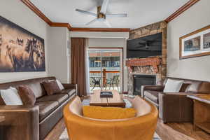 Living room with crown molding, a fireplace, wood finished floors, and a ceiling fan
