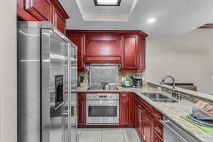 Kitchen featuring reddish brown cabinets, appliances with stainless steel finishes, a textured ceiling, light stone counters, and decorative backsplash