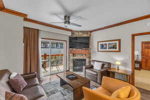 Living area featuring crown molding, a fireplace, wood finished floors, ceiling fan, and a textured ceiling