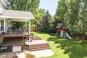 Fenced backyard featuring a playground, a deck, view of wooded area, and a patio area