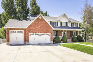 Traditional-style house featuring concrete driveway, an attached garage, covered porch, a shingled roof, and brick siding