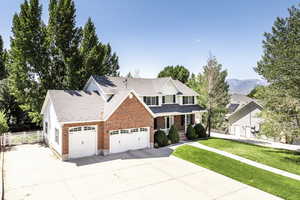Traditional home featuring a garage, concrete driveway, covered porch, brick siding, and a shingled roof
