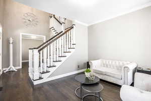 Living room with dark wood-type flooring, crown molding, and stairs