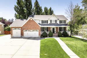 Traditional-style house with a front lawn, a porch, an attached garage, and concrete driveway