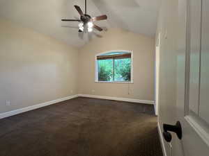 Empty room with vaulted ceiling, dark colored carpet, and a ceiling fan