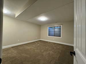 Unfurnished room with a textured ceiling and dark colored carpet