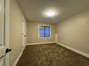Unfurnished room with dark carpet and a textured ceiling