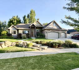 View of front of property with a front lawn, an attached garage, stone siding, and driveway