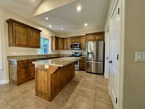Kitchen with brown cabinets, stainless steel appliances, light stone counters, recessed lighting, and a center island
