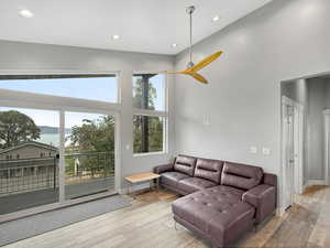 Living room with a water view, recessed lighting, light wood-style floors, a ceiling fan, and a towering ceiling