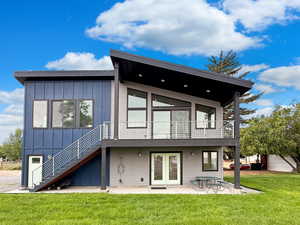 Back of property featuring board and batten siding, stairs, a patio area, a lawn, and french doors
