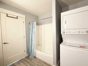 Full bathroom featuring shower / tub combo with curtain, light wood-style floors, and stacked washer / dryer