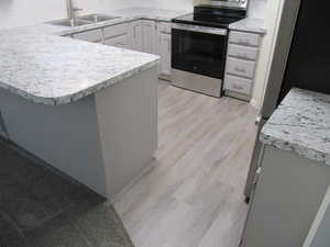 Kitchen featuring stainless steel electric stove, light countertops, light wood-style floors, a peninsula, and gray cabinets