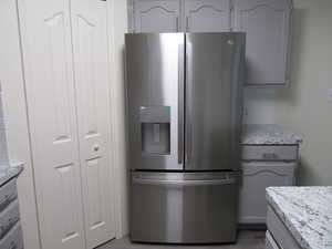 Kitchen with stainless steel fridge, gray cabinetry, light stone counters, decorative backsplash, and light wood-type flooring