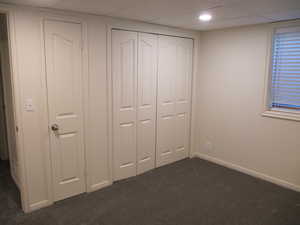 Unfurnished bedroom with a drop ceiling, dark colored carpet, and a closet