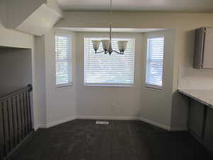 Unfurnished dining area with healthy amount of natural light, dark colored carpet, and a chandelier