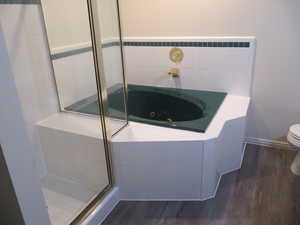 Bathroom featuring dark wood finished floors, a stall shower, and a tub with jets
