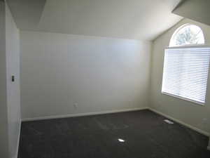 Unfurnished room featuring dark carpet and vaulted ceiling