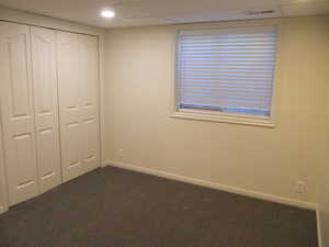 Unfurnished bedroom featuring dark colored carpet, a closet, and a paneled ceiling