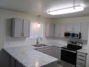 Kitchen with gray cabinets, stainless steel appliances, decorative light fixtures, a peninsula, and decorative backsplash