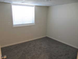 Empty room featuring dark colored carpet and a drop ceiling