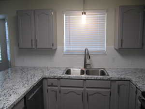 Kitchen featuring gray cabinets, decorative light fixtures, dishwasher, tasteful backsplash, and light stone countertops