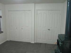 Bedroom with dark colored carpet, a wood stove, and multiple closets