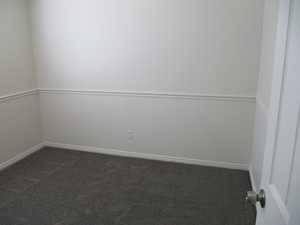 Unfurnished room featuring dark carpet and baseboards