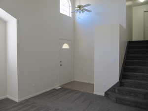 Foyer featuring stairway, dark colored carpet, ceiling fan, and a high ceiling