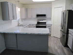 Kitchen with stainless steel appliances, gray cabinets, light countertops, and a peninsula