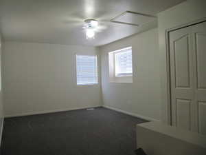 Spare room with dark carpet, attic access, and ceiling fan