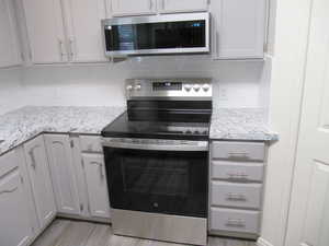 Kitchen featuring stainless steel appliances, decorative backsplash, light stone counters, and white cabinetry