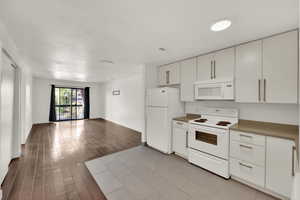 Kitchen with white appliances, white cabinetry, light wood-type flooring, open floor plan, and light countertops