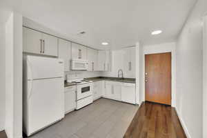 Kitchen with white appliances, white cabinets, dark countertops, recessed lighting, and dark wood-style flooring