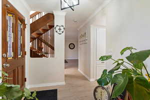 Entrance foyer with ornamental molding, light wood-type flooring, and stairs