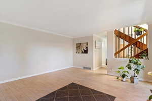 Unfurnished living room with crown molding, light wood finished floors, and stairs