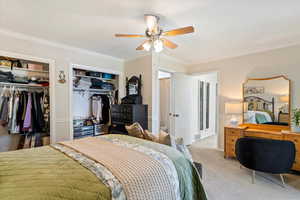 Carpeted bedroom with ornamental molding, two closets, and ceiling fan
