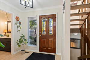 Foyer with crown molding, light wood finished floors, and a chandelier