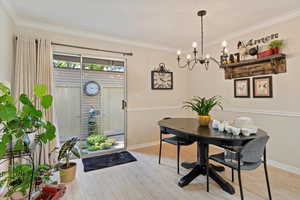 Dining space with wood finished floors, crown molding, and a chandelier