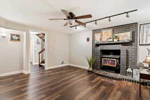 Unfurnished living room featuring rail lighting, dark wood-style flooring, a ceiling fan, and a fireplace