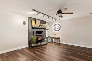 Living area featuring rail lighting, dark wood-type flooring, ceiling fan, and a fireplace