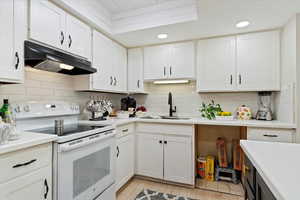Kitchen featuring white electric range oven, white cabinets, under cabinet range hood, tasteful backsplash, and recessed lighting