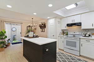 Kitchen featuring white range with electric stovetop, backsplash, light countertops, white cabinets, and hanging light fixtures