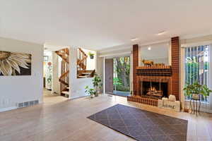 Living room with light wood-style flooring, healthy amount of natural light, stairs, and a brick fireplace