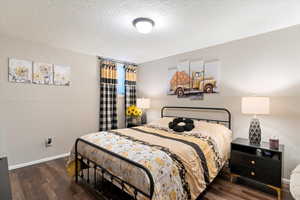 Bedroom with a textured wall, a textured ceiling, and dark wood-type flooring
