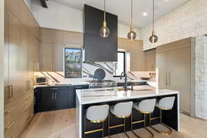 Kitchen featuring dark cabinetry, light wood-type flooring, decorative light fixtures, a kitchen bar, and modern cabinets