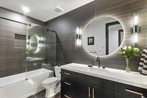 Bathroom with shower / bath combination with glass door, tile walls, vanity, and dark tile patterned floors