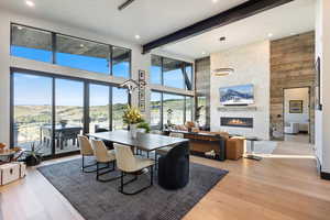 Dining room featuring a towering ceiling, a stone fireplace, light wood-style floors, beam ceiling, and recessed lighting