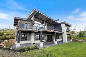 Rear view of house with a patio area, a yard, stone siding, and a balcony