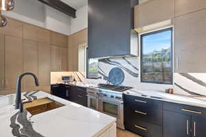 Kitchen featuring dark cabinetry, light stone countertops, range with two ovens, and modern cabinets